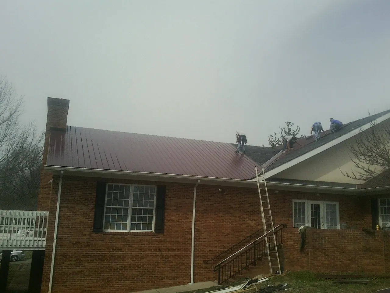 Crew setting red metal roofing panels on a brick home in Tipton